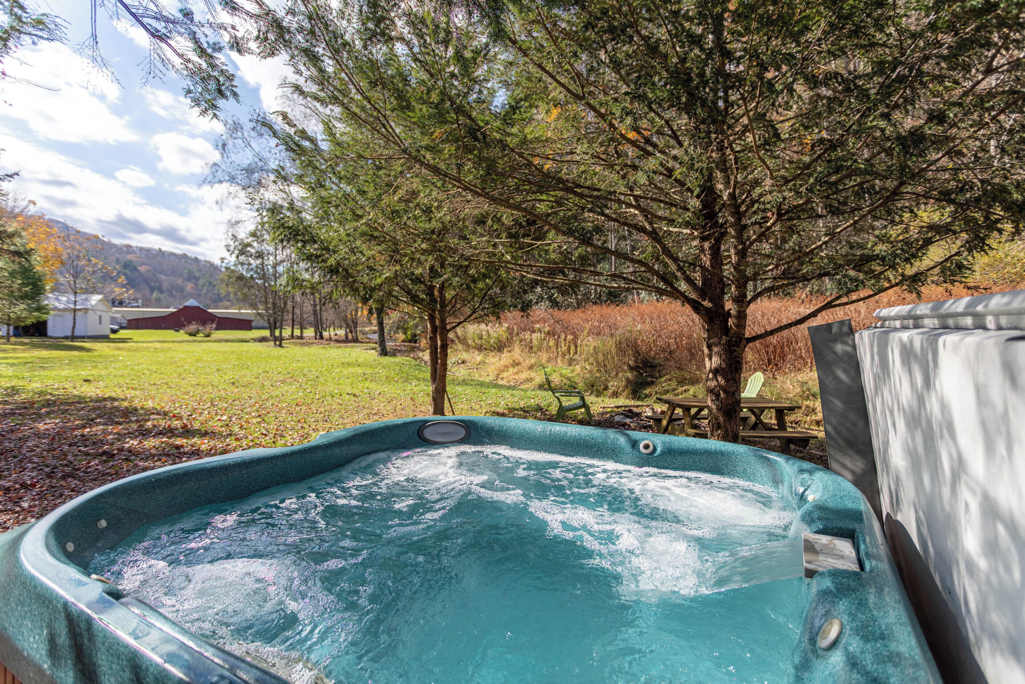 A hot tub in a backyard with a tree, a picnic table, and a red barn in the background.