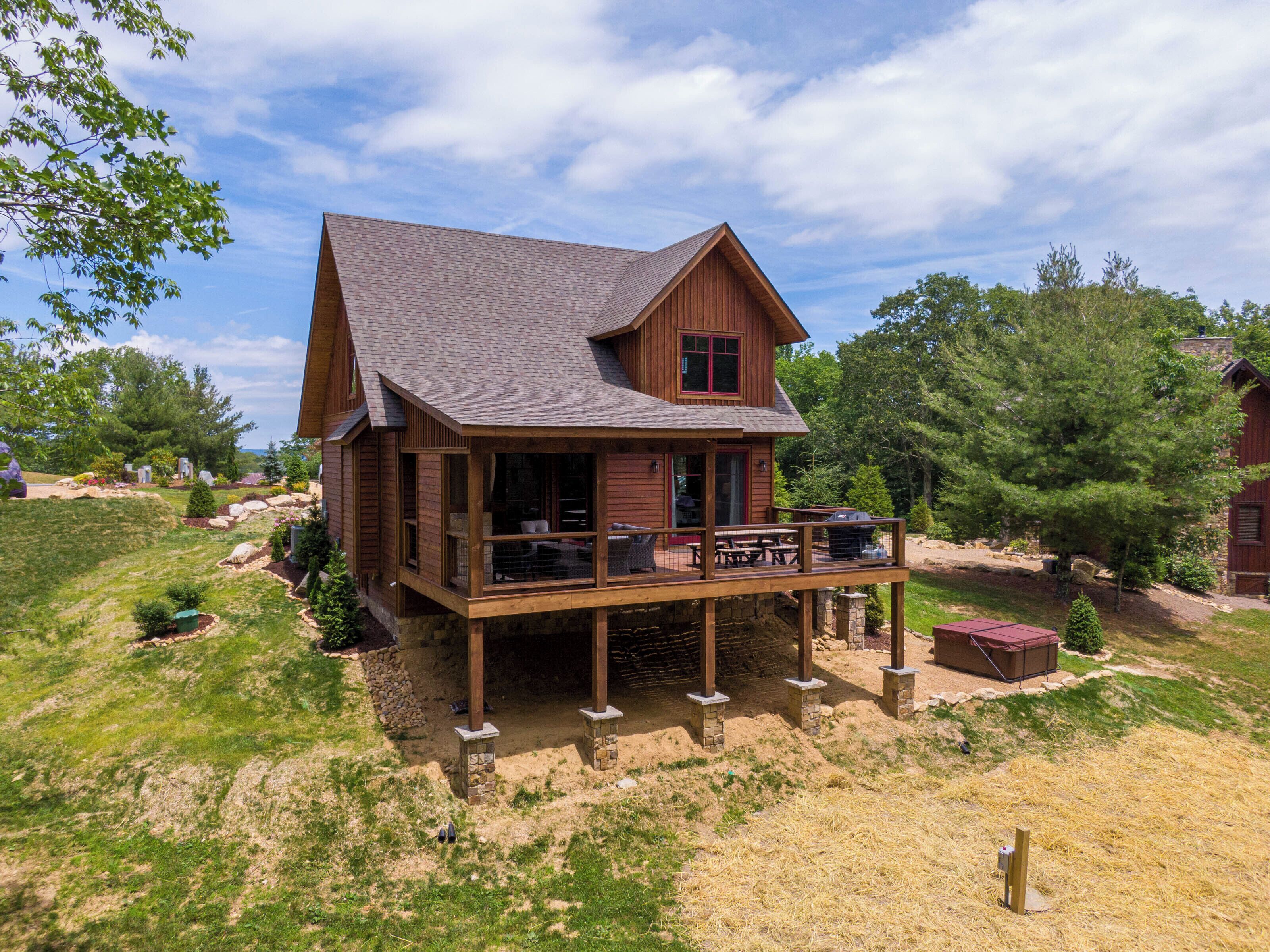 Een houten chalet met terras, omringd door een aangelegde tuin met bomen en rotsen.