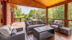 Una terraza cubierta de madera con muebles de mimbre, incluyendo un sofá y sillas, y una parrilla.
