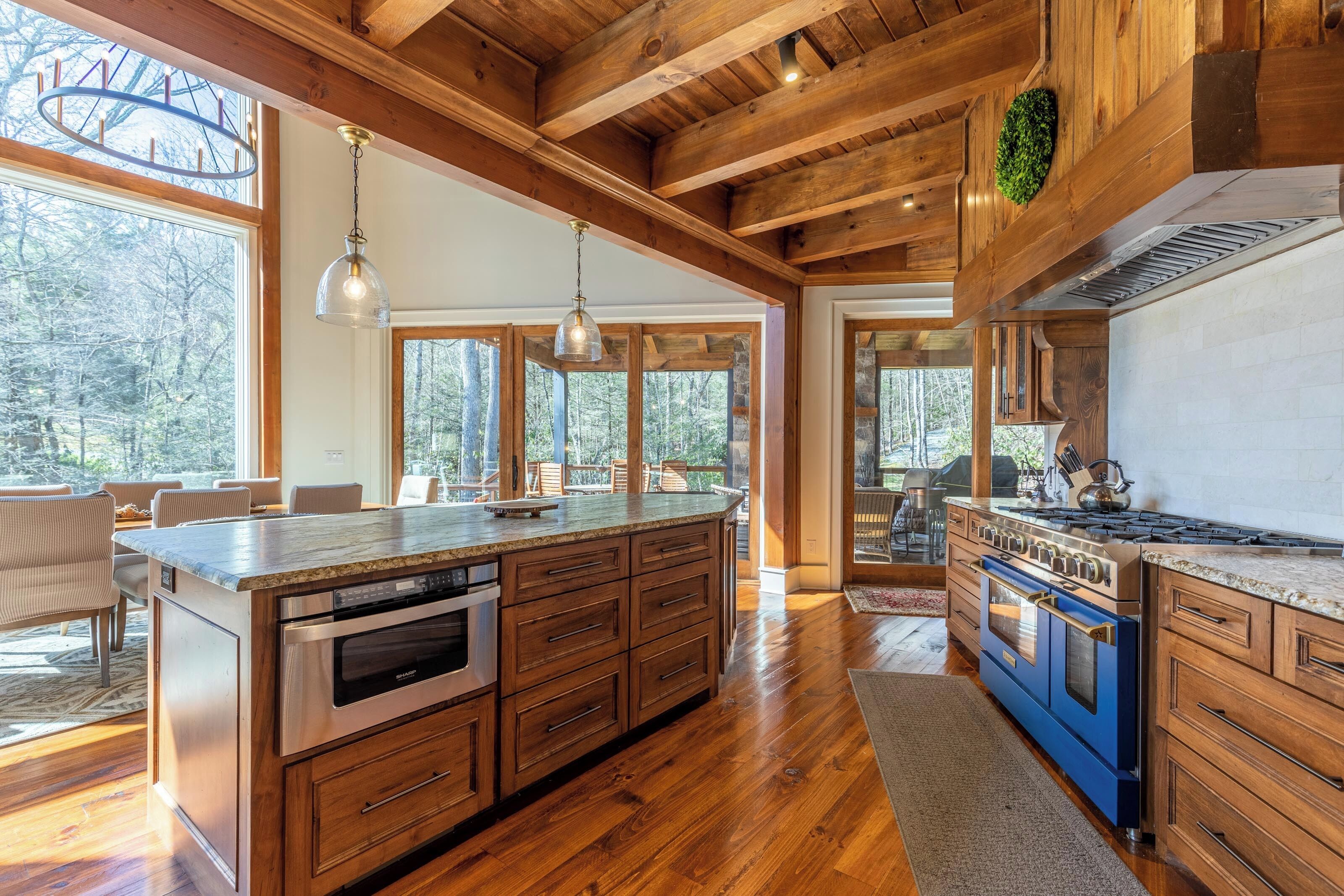 A spacious kitchen with wooden beams, large windows, and a central island with a built-in oven.