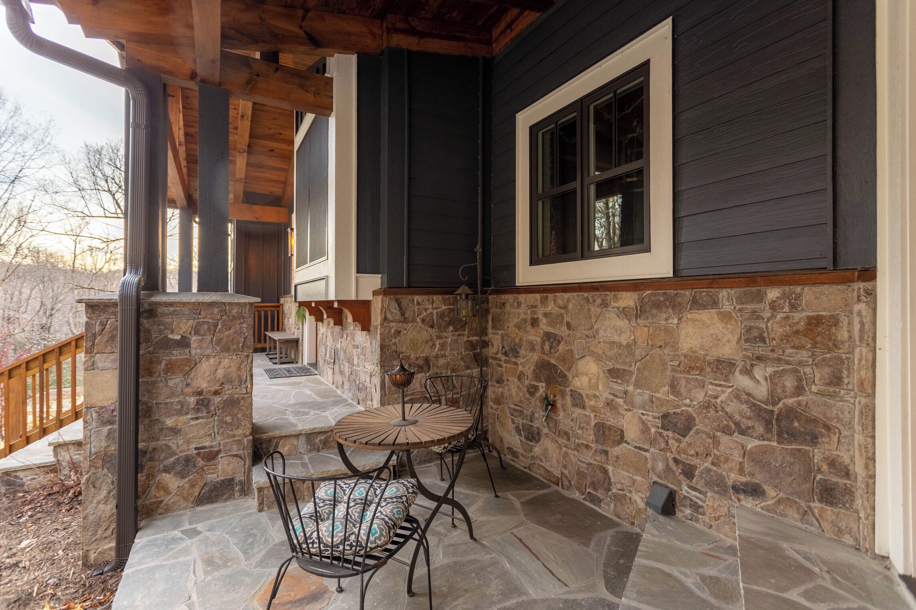 A stone patio with a table and chairs, a wooden deck, and a stone wall.