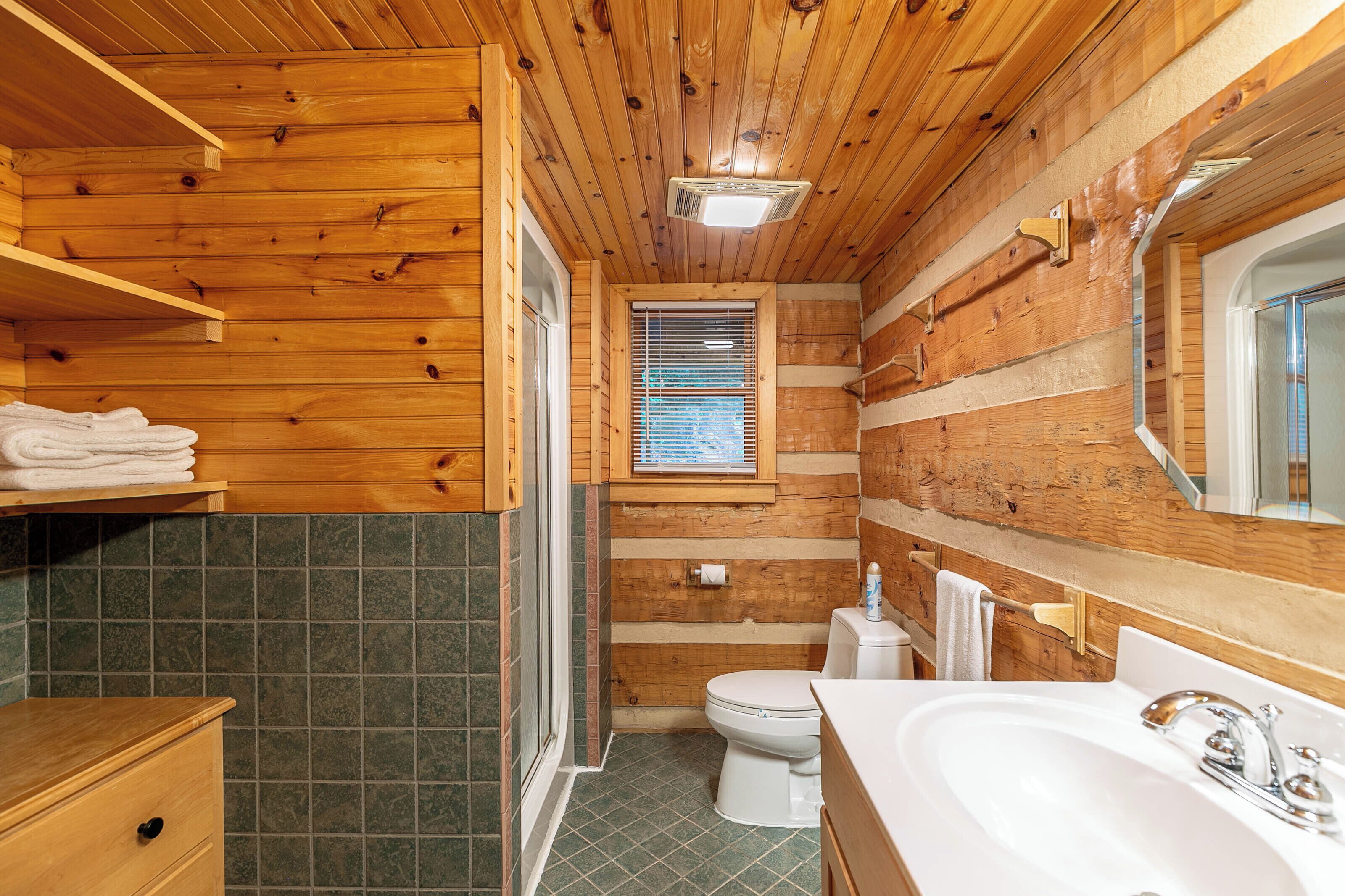 A wooden-paneled bathroom with a toilet, sink, and shower.