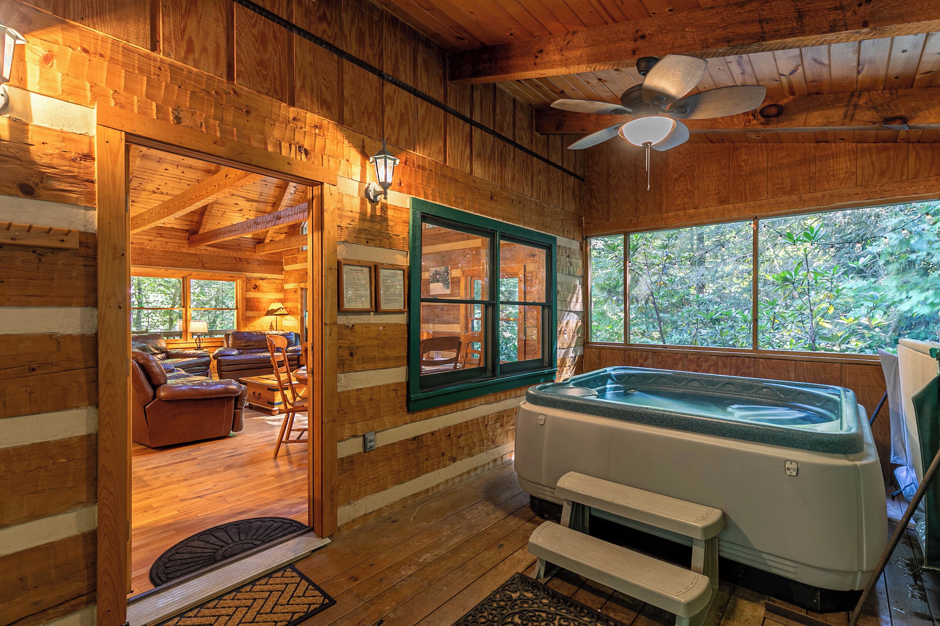 A wooden cabin interior with a hot tub, seating area, and large windows offering a view of the outdoors.