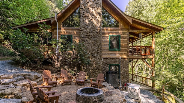 A rustic cabin with a stone chimney, wooden deck, Adirondack chairs, and a fire pit. - Skylark - Cozy Log Cabin With 3 Bedrooms, and hot Tub- (Banner Elk)
