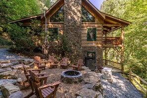 Eine rustikale Holzhütte mit einem Steinkamin, einer Holzterrasse, Adirondack-Stühlen und einer Feuerstelle.