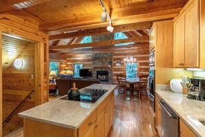Ein rustikales Blockhaus-Interieur mit Kamin aus Stein, Esstisch aus Holz und einer Küchenzeile mit Herd.