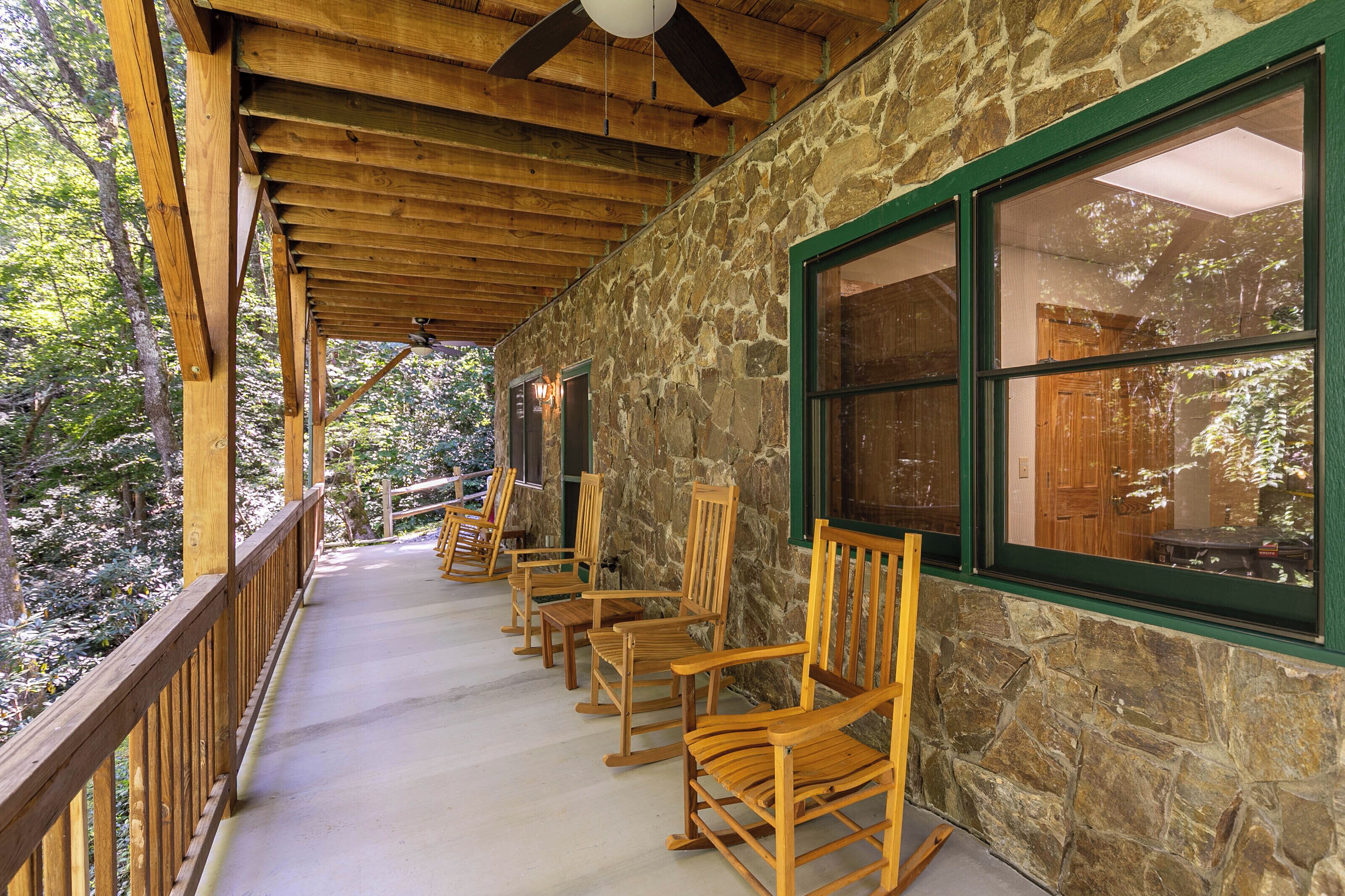A covered porch with wooden rocking chairs, stone walls, and large windows.