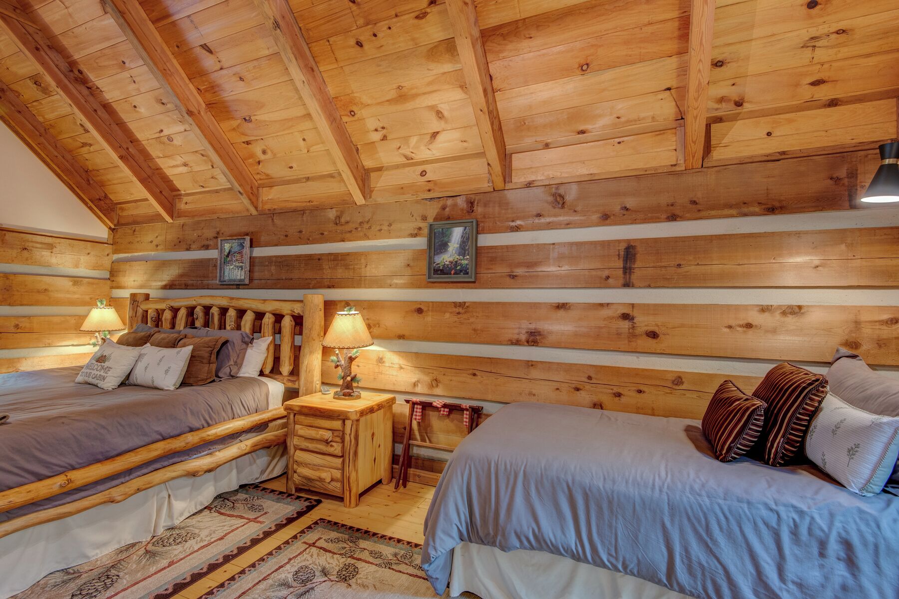 A log cabin bedroom with two beds, wooden headboard, a nightstand, and a small table.