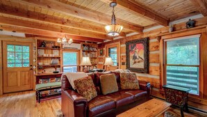 A cozy cabin interior with a wooden ceiling, a leather sofa, a dining table, and a bookshelf filled with books and decorative items. - Casa Haven (Boone)
