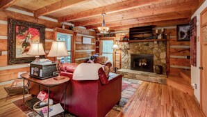 A cozy log cabin interior with a fireplace, leather sofa, and rustic decor. - Casa Haven (Boone)