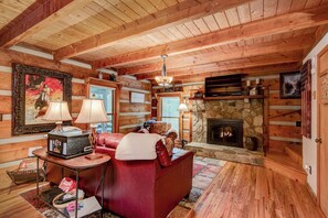 A cozy log cabin interior with a fireplace, leather sofa, and rustic decor. - Casa Haven (Boone)