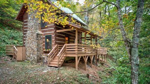 A rustic cabin with a stone foundation, wooden exterior, and a porch with steps leading to a deck. - Casa Haven (Boone)