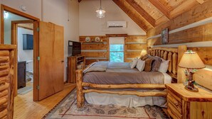 A log cabin bedroom with a bed, bedside table, lamp, and a window. - Casa Haven (Boone)