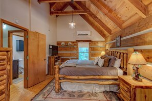 A log cabin bedroom with a bed, bedside table, lamp, and a window. - Casa Haven (Boone)