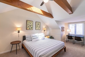 A bedroom with a large bed, two wall-mounted lamps, a desk with a chair, and a window with blinds.
