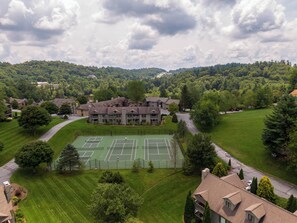 A large building with a tennis court, surrounded by lush greenery and a hilly landscape. - Chetola Chestnut 8 (Blowing Rock)