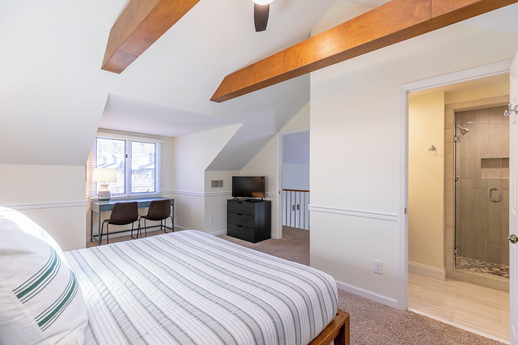 A bedroom with a bed, a desk, and a TV. There is a door leading to a bathroom.