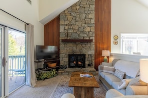 Una sala de estar con chimenea de piedra, televisor, sofá y mesa de centro.