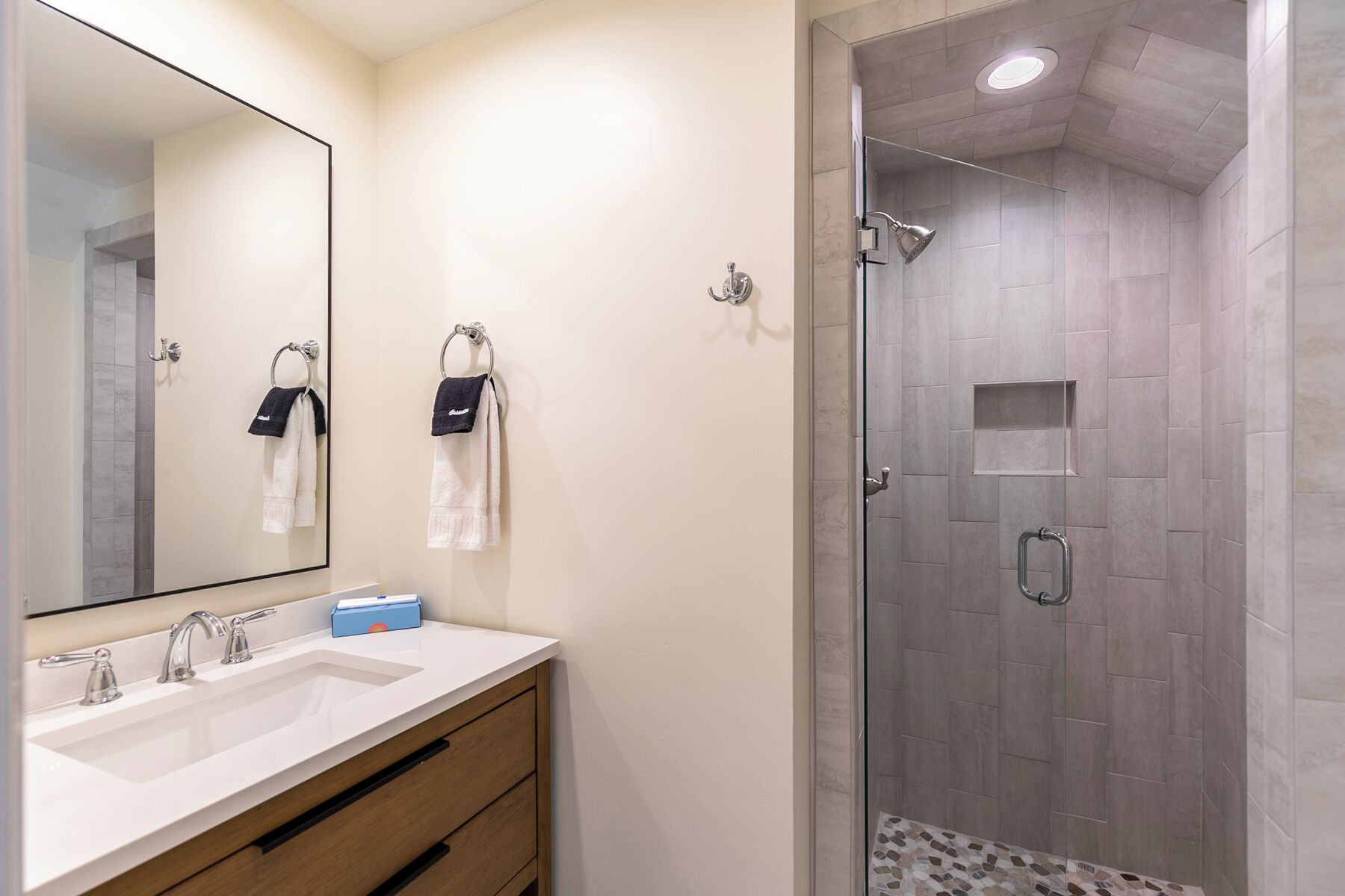 Une salle de bain dotée d’un grand miroir, de deux lavabos et d’un espace douche avec une porte en verre.