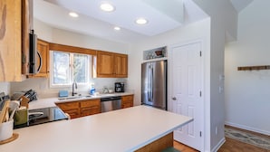 A modern kitchen with wooden cabinets, a stainless steel refrigerator, and a white countertop.