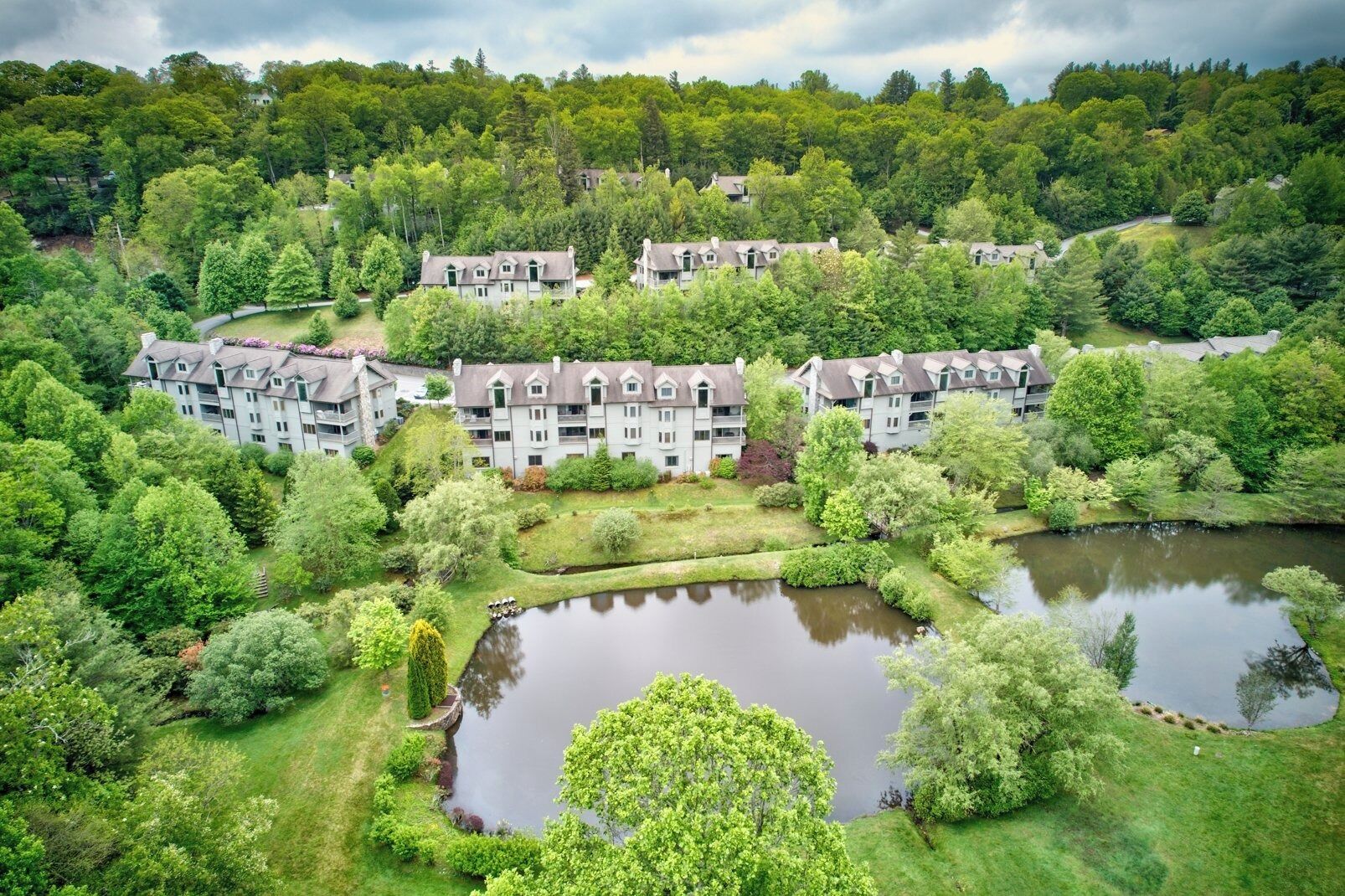 A multi-story residential building with a central courtyard, surrounded by lush greenery and a small pond.