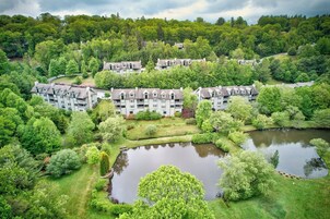 A multi-story residential building with a central courtyard, surrounded by lush greenery and a small pond.