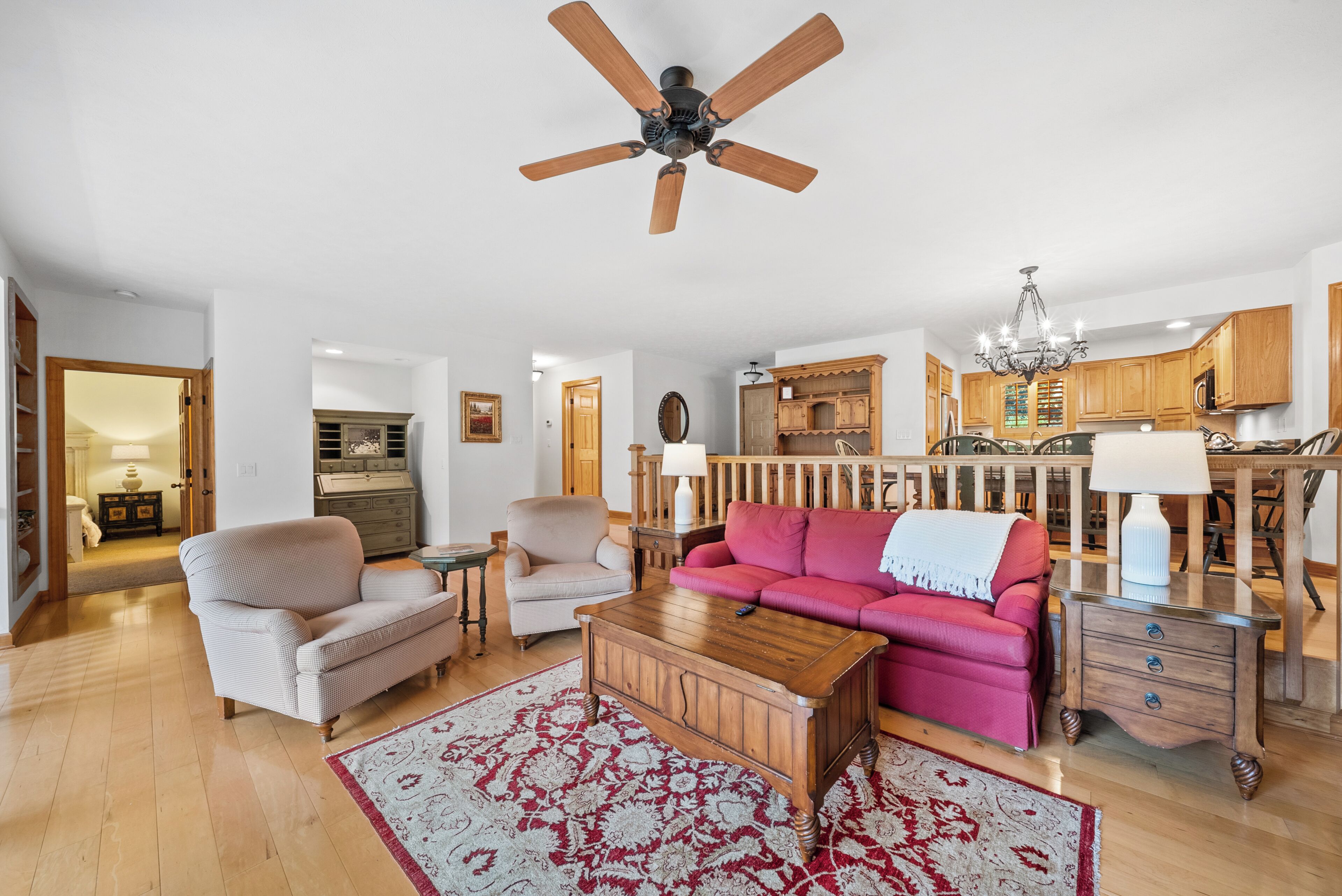A living room with a ceiling fan, a red sofa, a wooden coffee table, and a patterned rug.