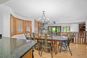 A dining area with a granite countertop, wooden chairs, a wooden dining table, a chandelier, and a view of the outdoors.