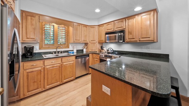 A kitchen with wooden cabinets, stainless steel appliances, a granite countertop, and recessed ceiling lights.