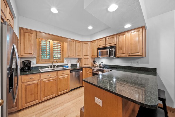 A kitchen with wooden cabinets, stainless steel appliances, a granite countertop, and recessed ceiling lights.