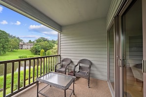 Un balcon avec une table et deux chaises, une porte vitrée et une vue sur un immeuble et de la verdure.