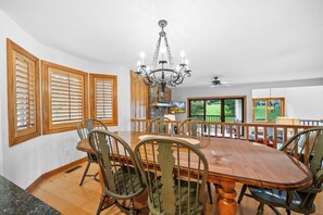 A dining room with a wooden table, chairs, a chandelier, and large windows with blinds. - Chetola Sierra 1 (Blowing Rock)