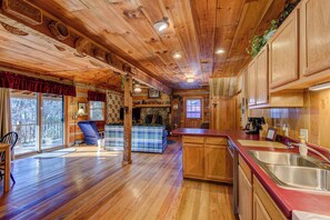 Interior de una cabaña de madera con cocina, comedor y una sala de estar acogedora con chimenea.