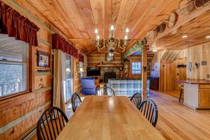 Interior de una cabaña de madera con una mesa de comedor, sillas, chimenea y televisor.