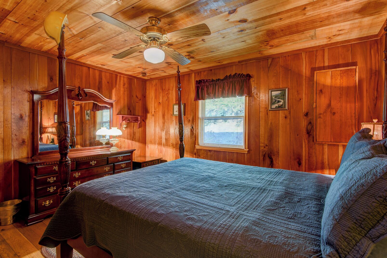 Quarto de cabana de madeira com cama de dossel, ventilador de teto e janela com persianas.
