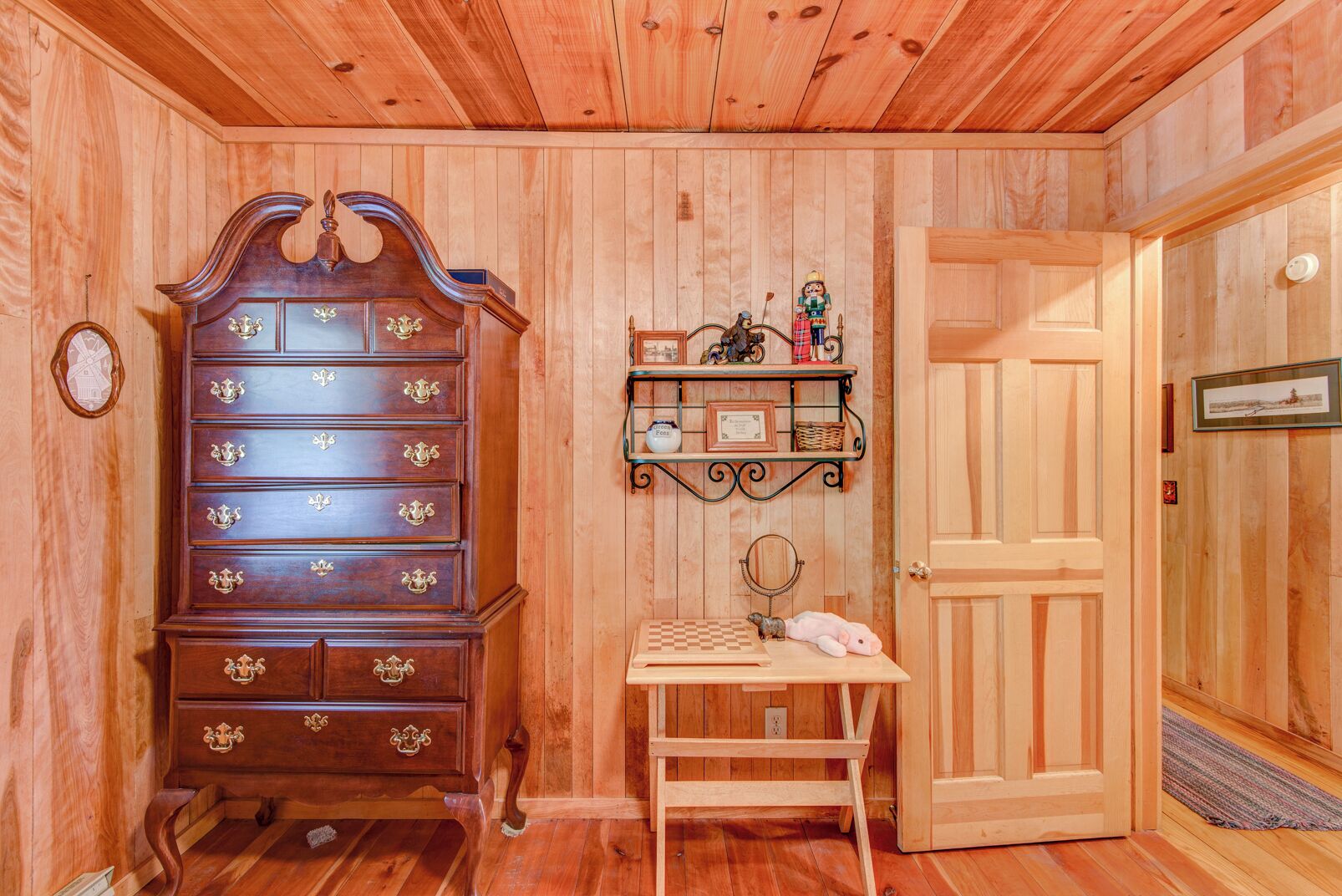 Ein Zimmer mit Holzwänden, einer großen Holzkommode, einem kleinen Tisch mit Spiegel und einer Tür.