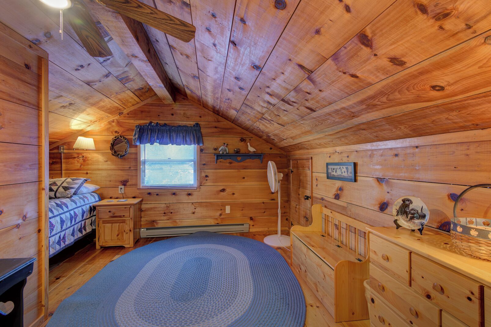 Una habitación acogedora tipo cabaña con cama, cómoda y ventana con persianas.