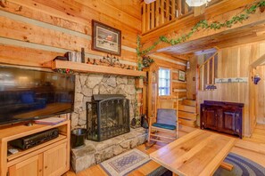 Un interior de cabaña acogedor con chimenea de piedra, paredes de madera, un televisor y un comedor.