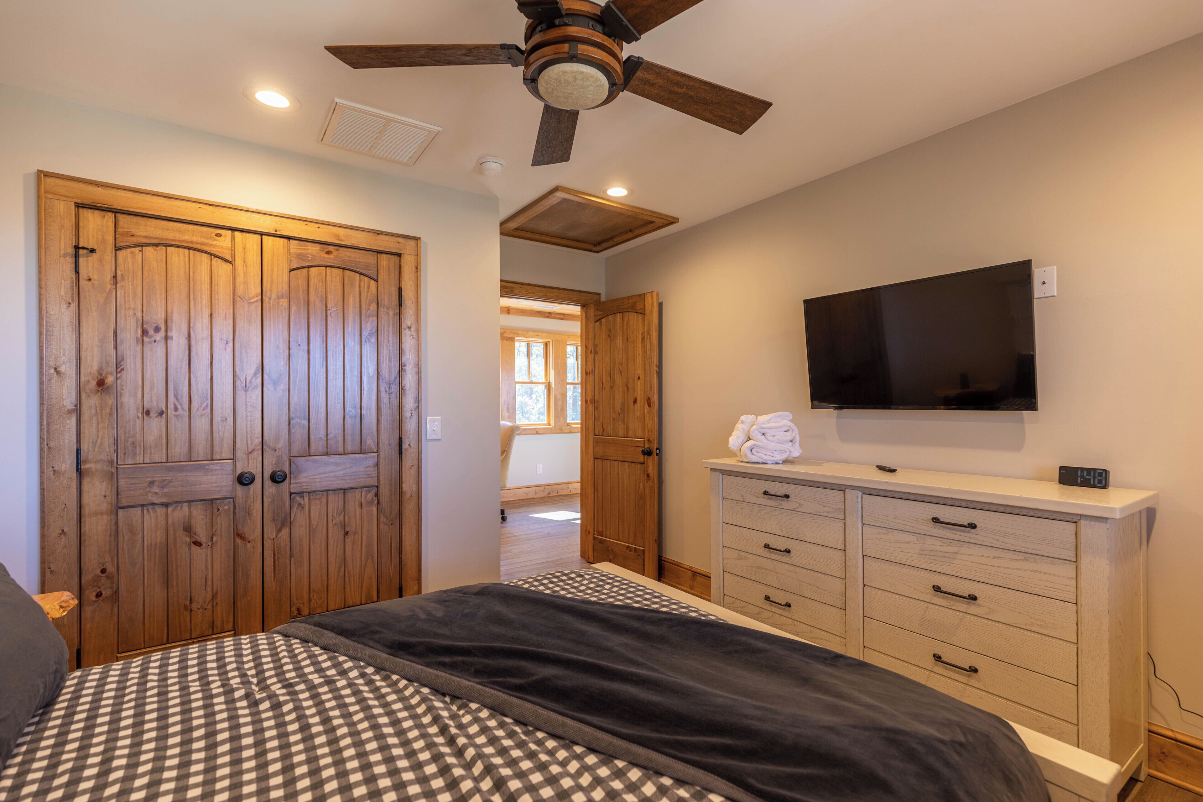 A bedroom with a bed, wooden wardrobe, a television, and a ceiling fan.