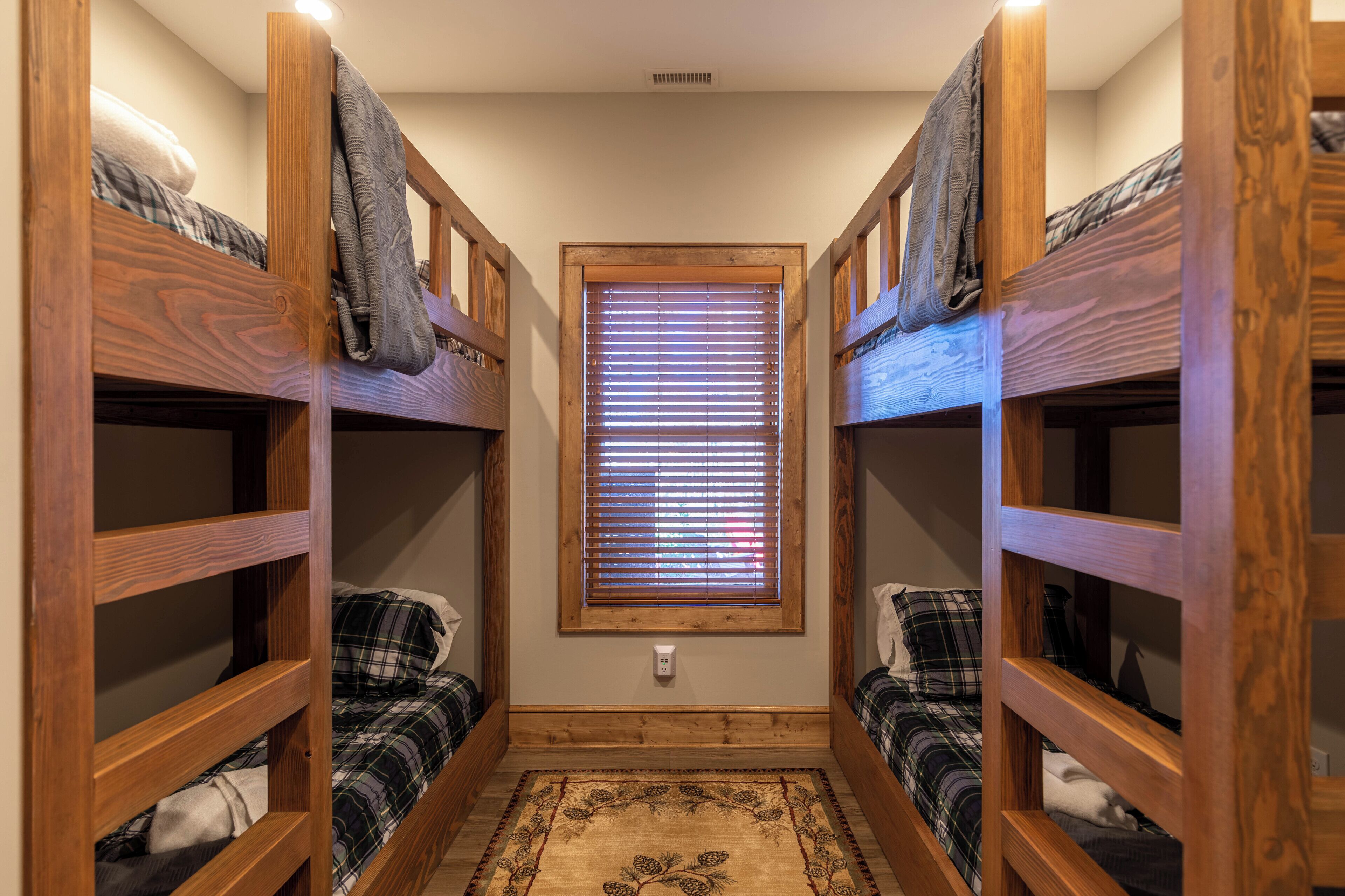 A narrow room with two bunk beds, a window with blinds, and a small rug.