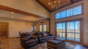 A spacious living room with leather sofas, a large window, and a high ceiling with exposed beams. - Hidden Gem at Eagles Nest (Banner Elk)