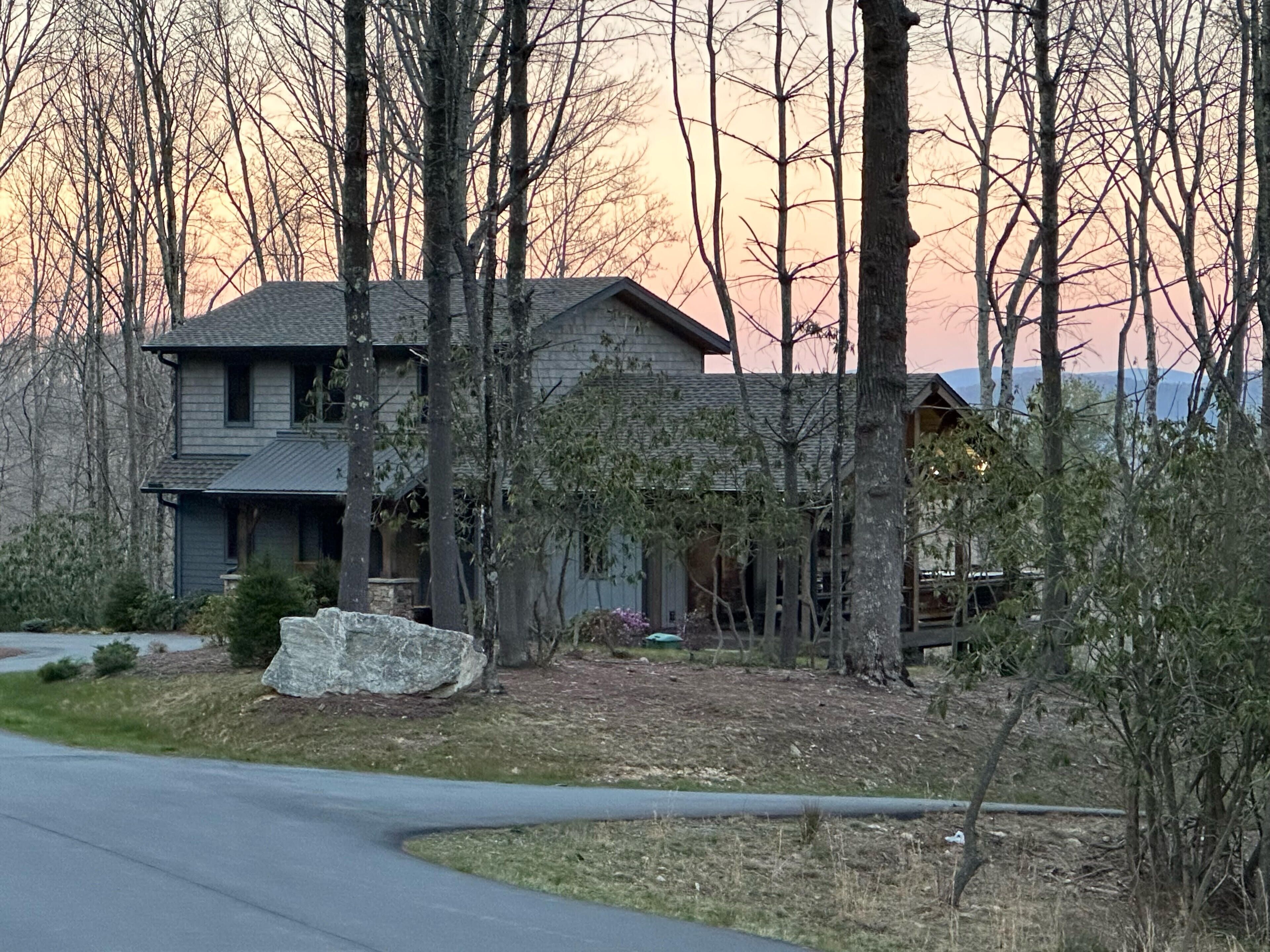A two-story house with a stone foundation, surrounded by trees and a clear sky.
