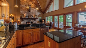 A spacious kitchen with wooden cabinets, a stone fireplace, and a large island. - The Boulders - 5BR With Hot Tub 50mi Views Pool Table Sauna Wet Bar Dog Friendly (Boone)