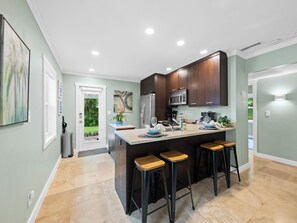Uma cozinha moderna com ilha central, banquetas e vista para o exterior.