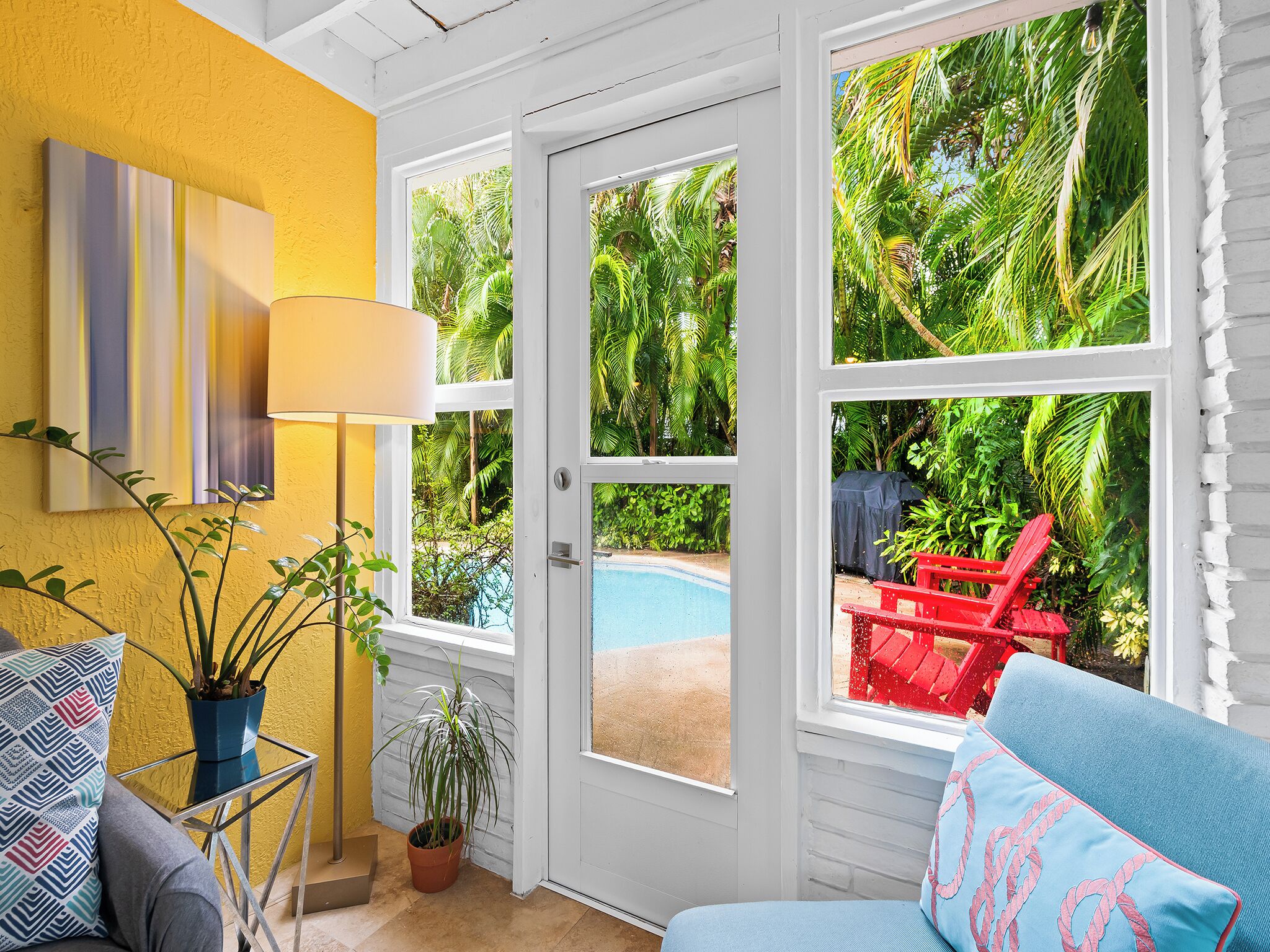 A bright room with a yellow wall, a large window, a pool, and a red chair outside.