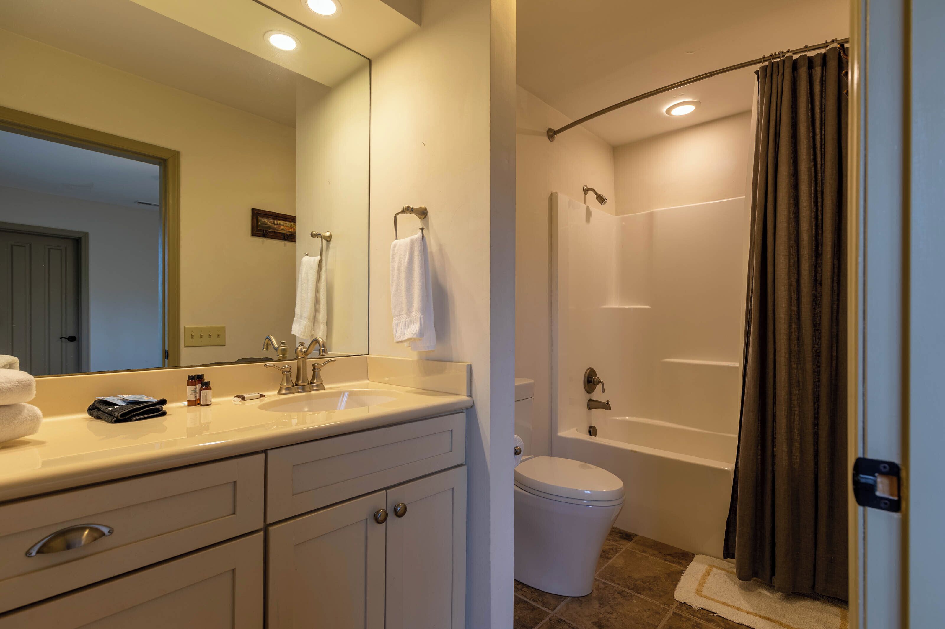 A bathroom with a sink, mirror, toilet, and shower.