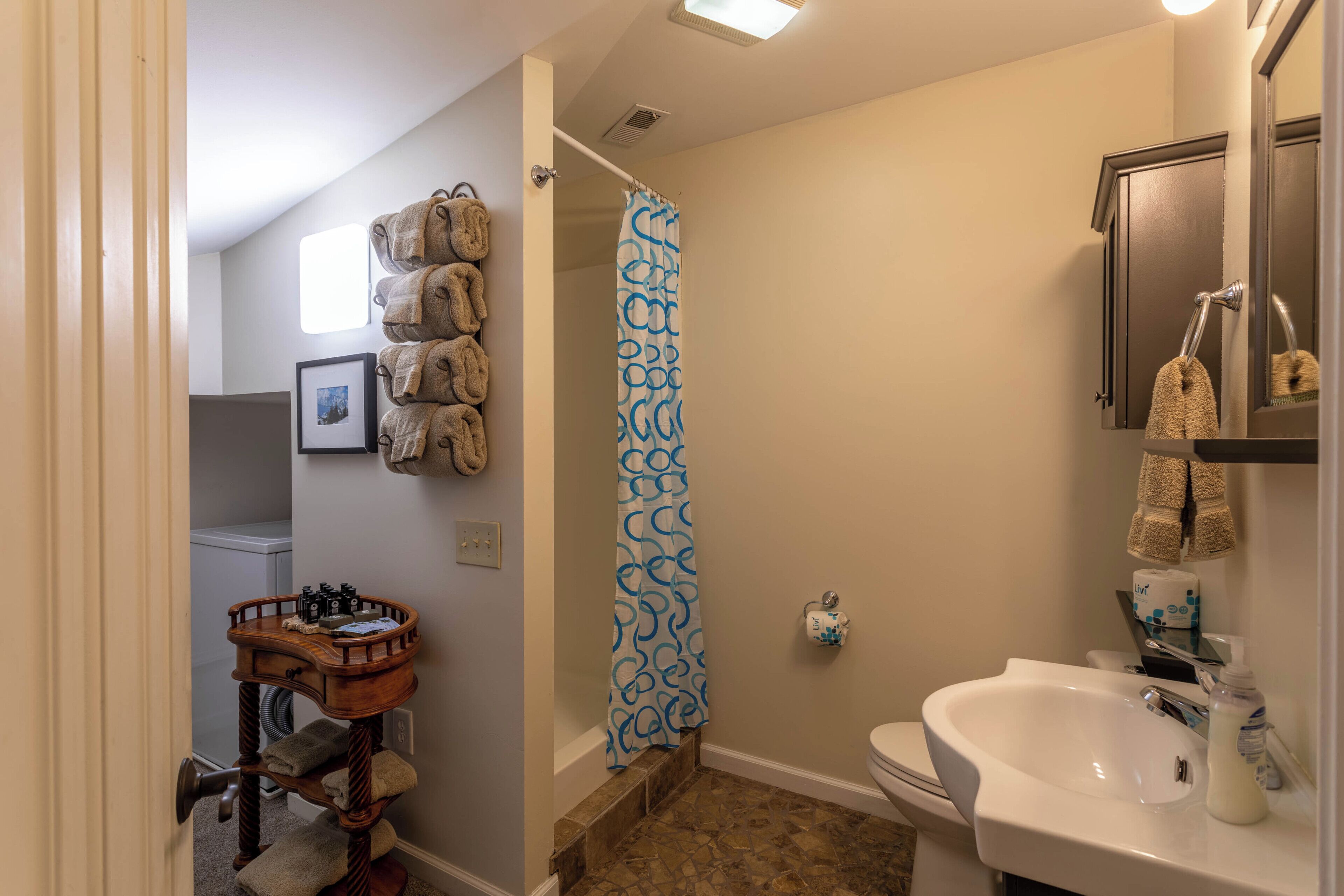 A bathroom with a shower, toilet, sink, and a small wooden side table with towels.