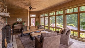 Un intérieur de chalet chaleureux avec un plafond en bois, de grandes fenêtres, une cheminée et un décor rustique.