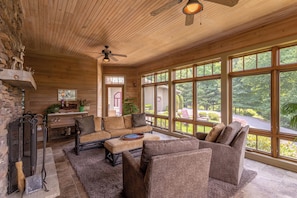 Ein gemütliches Blockhauss-Interieur mit Holzbalkendecke, großen Fenstern, Kamin und rustikalen Einrichtungsgegenständen.