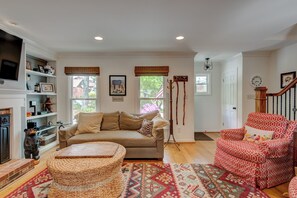 A cozy living room with a beige sofa, a red patterned armchair, a woven ottoman, and a red and beige patterned rug.